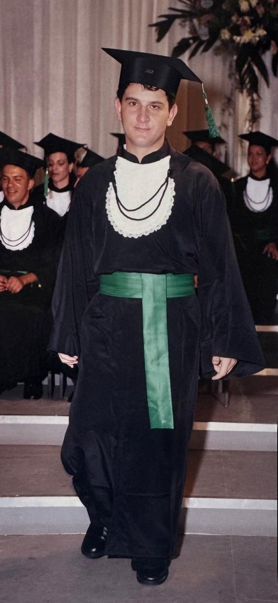 Dr. Sérgio Rodrigo Beraldo, de beca, capelo e faixa verde, desce os degraus do palco na cerimônia de colação de grau